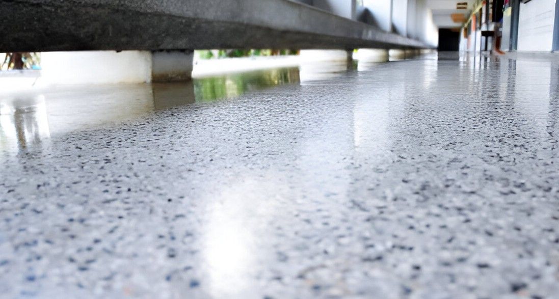 Polished concrete floor reflecting a bright light. White building columns and hallway in background.