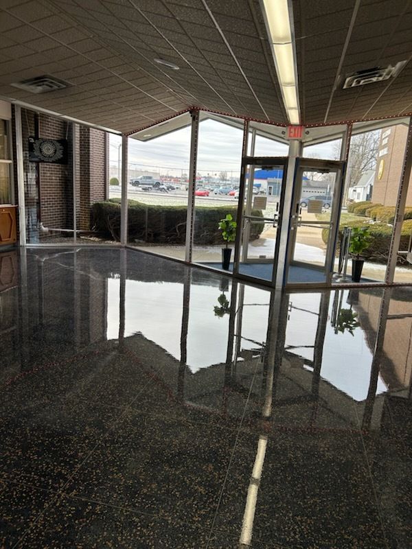 A brightly lit building lobby with a highly polished, reflective dark floor looking out onto a parking lot.
