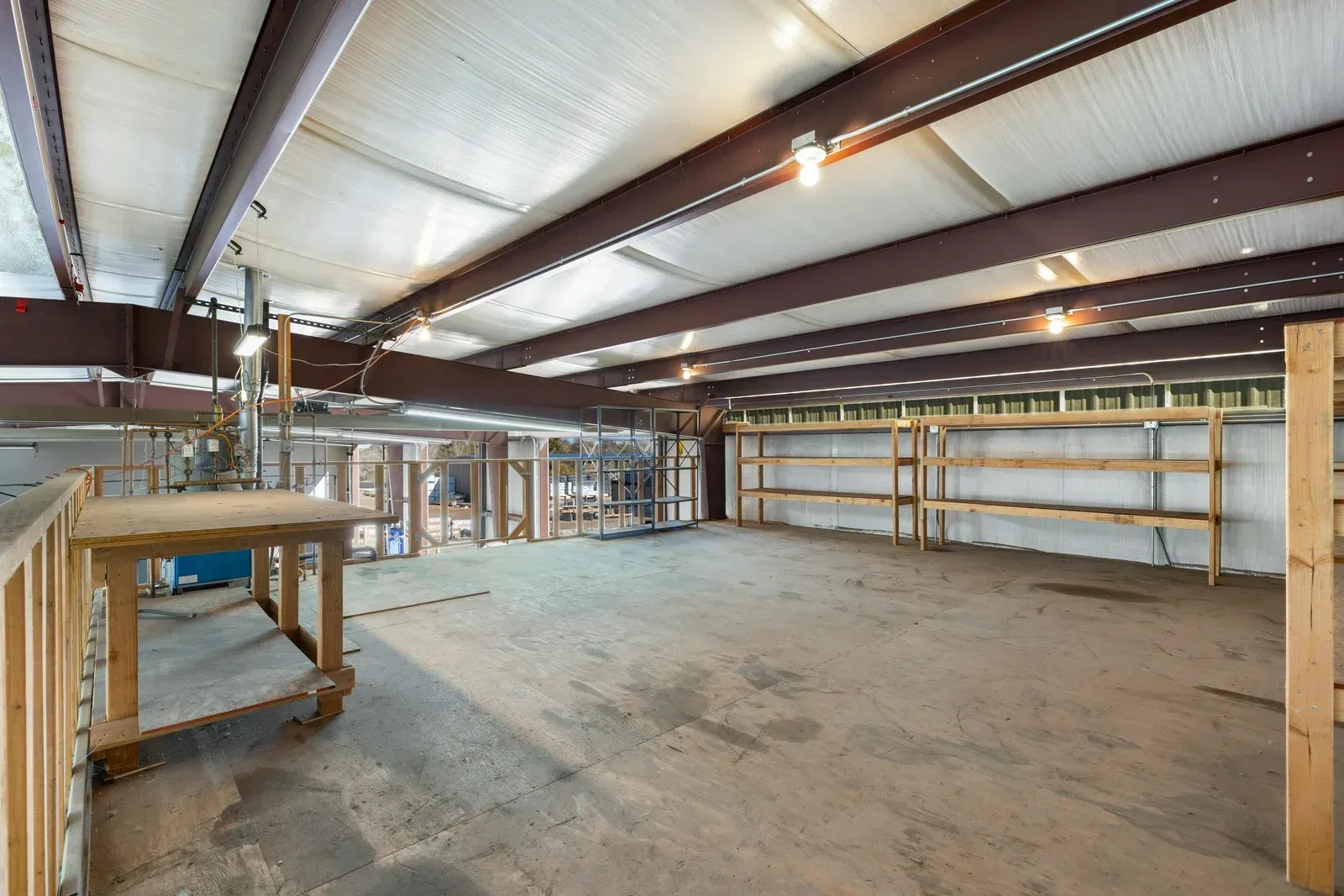 Interior of a large, empty metal building with worktable, shelving, and visible structural beams.