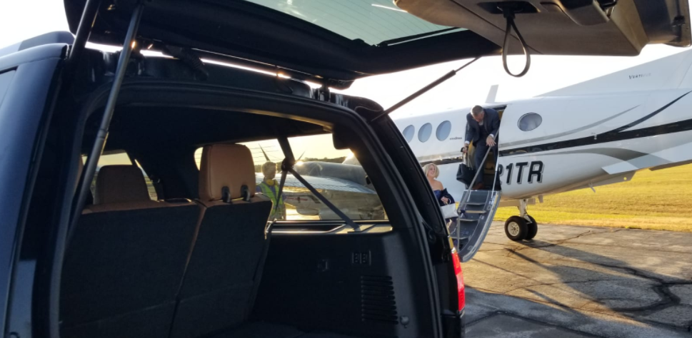 The back of a car is open and a plane is parked in the background.