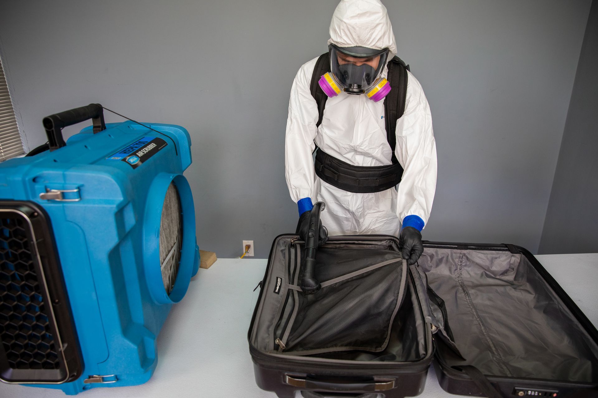 A man in a protective suit is opening a suitcase