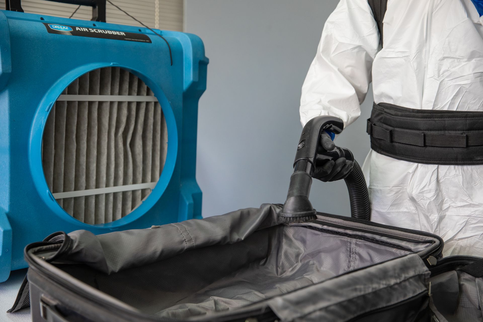 A man in a protective suit is cleaning a suitcase