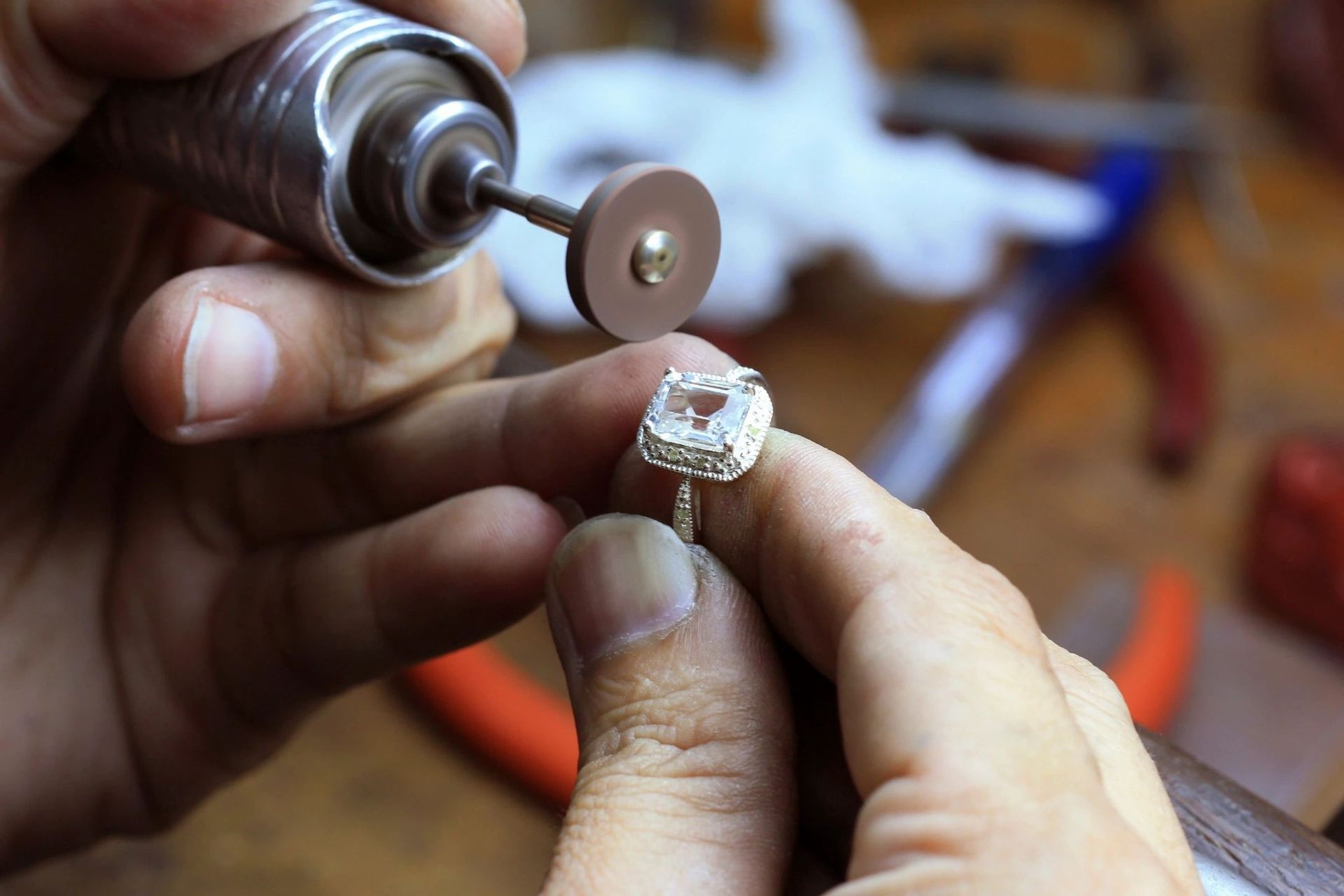 A jeweler uses a handheld rotary tool with a small polishing disc to refine a diamond engagement ring.
