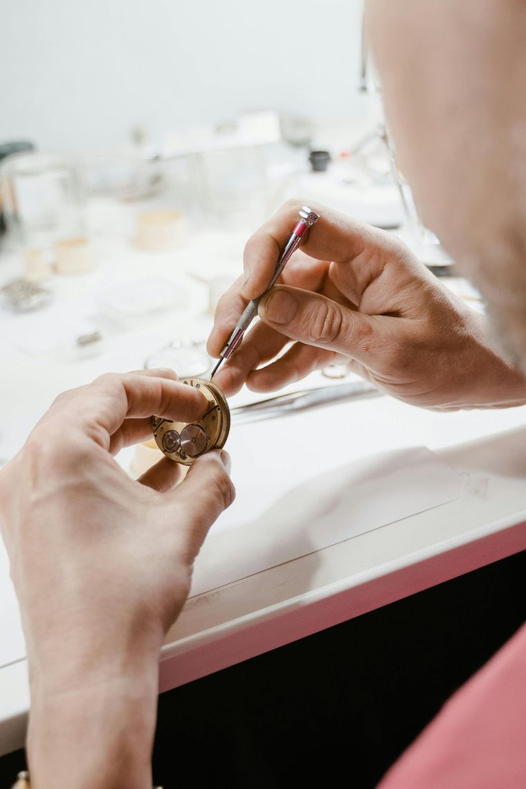 A watchmaker uses a fine screwdriver to perform precise mechanical work on a small, gold-colored watch movement.