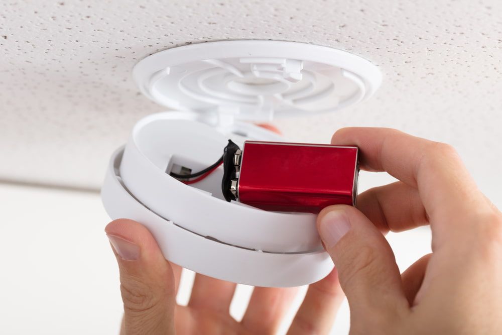 A Person Is Installing A Smoke Detector On The Ceiling  — Greg Keft Electrical in Wauchope, NSW