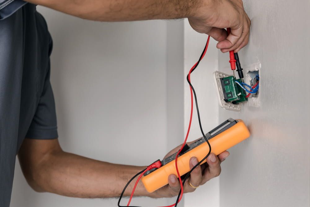 A Man Is Using A Multimeter To Test An Electrical Outlet — Greg Keft Electrical in Port Macquarie, NSW