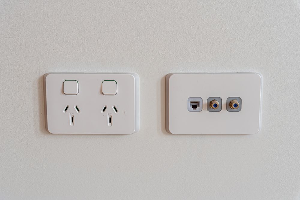 Two white electrical outlets and a light switch on a white wall  — Greg Keft Electrical in Wauchope, NSW