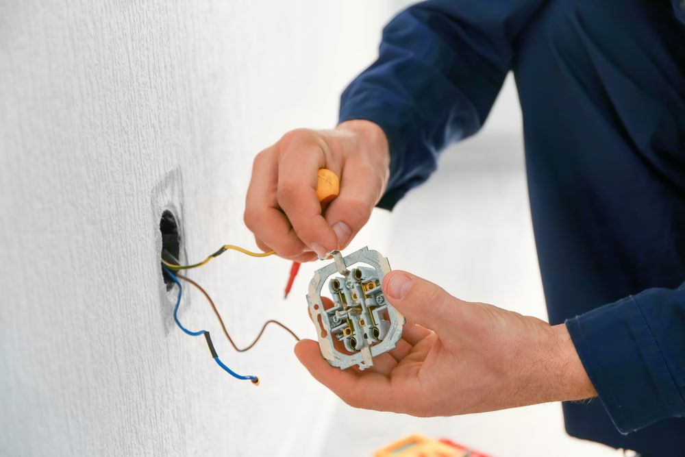 A Man Is Fixing An Electrical Outlet With A Screwdriver — Greg Keft Electrical in Lake Cathie, NSW