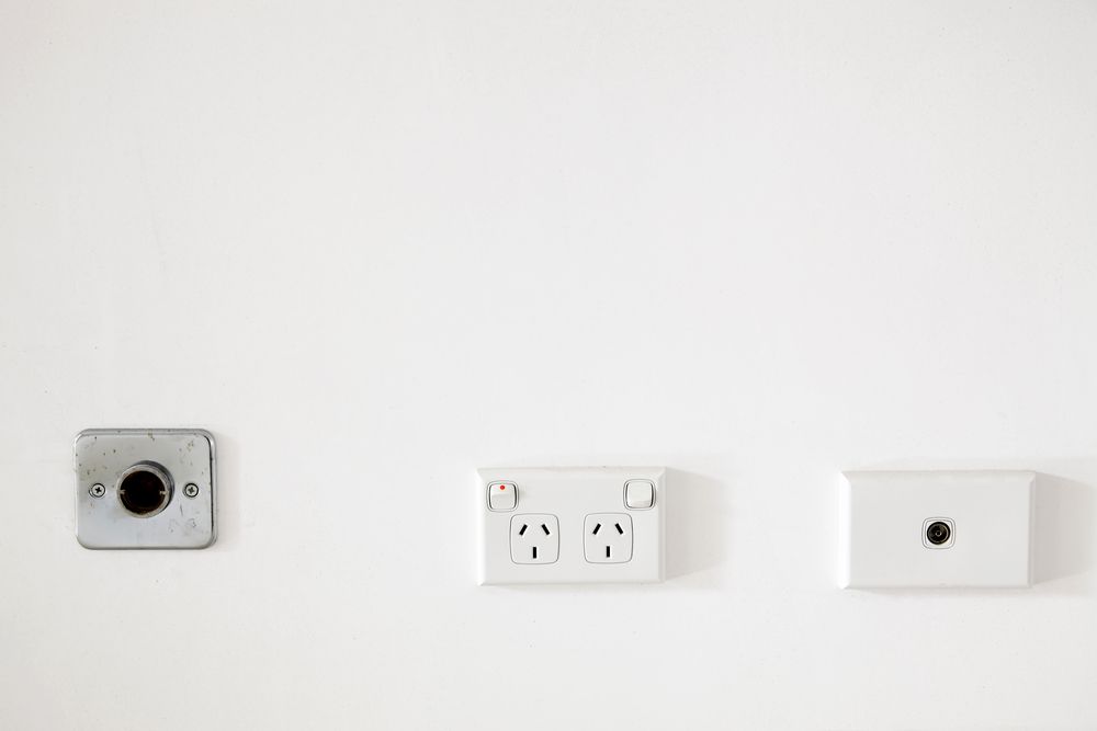 A white wall with three electrical outlets and a light switch — Greg Keft Electrical in Kempsey, NSW