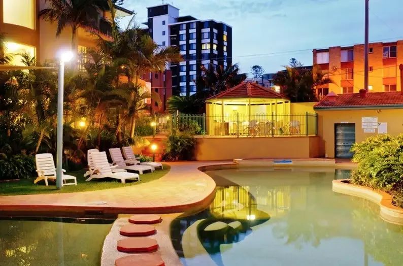 A Large Swimming Pool Is Surrounded By Chairs And Buildings At Night — Greg Keft Electrical in Port Macquarie, NSW