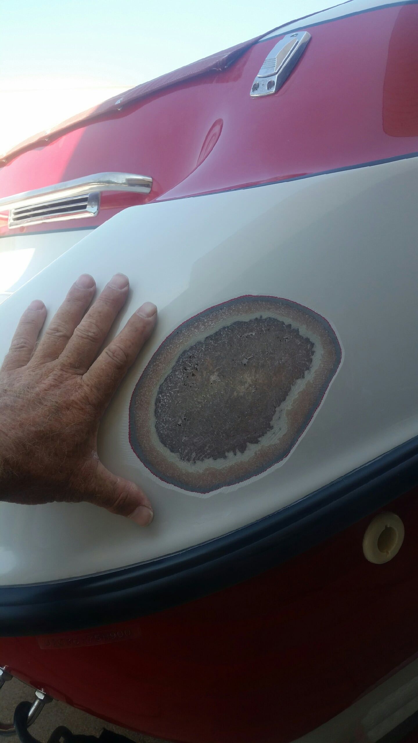 A person 's hand is on the side of a red and white boat.