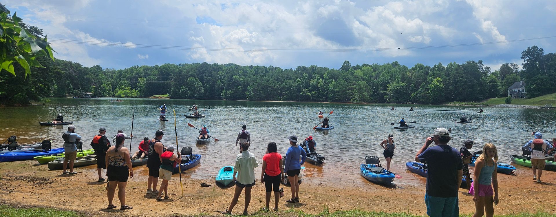 People with kayaks at a lake with trees and cloudy sky.