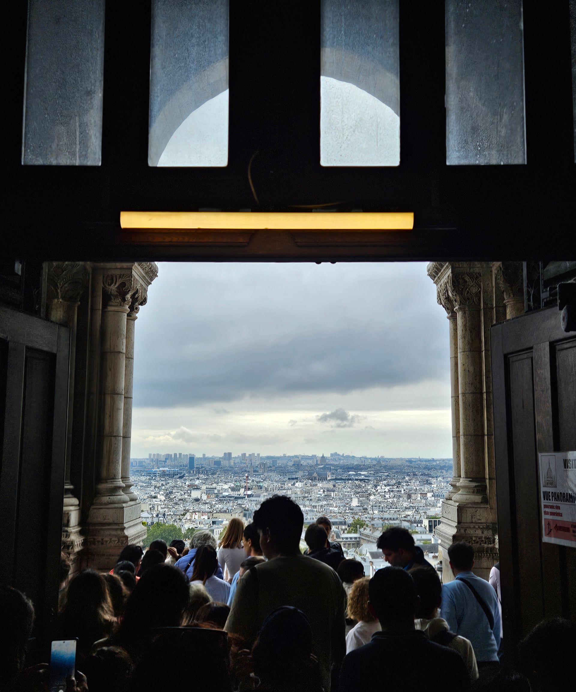 People at an open doorway looking at a cityscape under a cloudy sky.