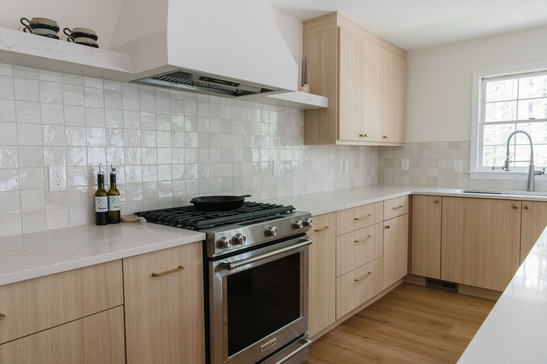 Light wood kitchen with white backsplash, stainless steel appliances, and white countertops.