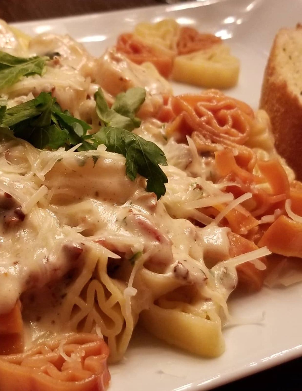 Pasta with creamy sauce, garnished with parsley and cheese, with bread on the side.