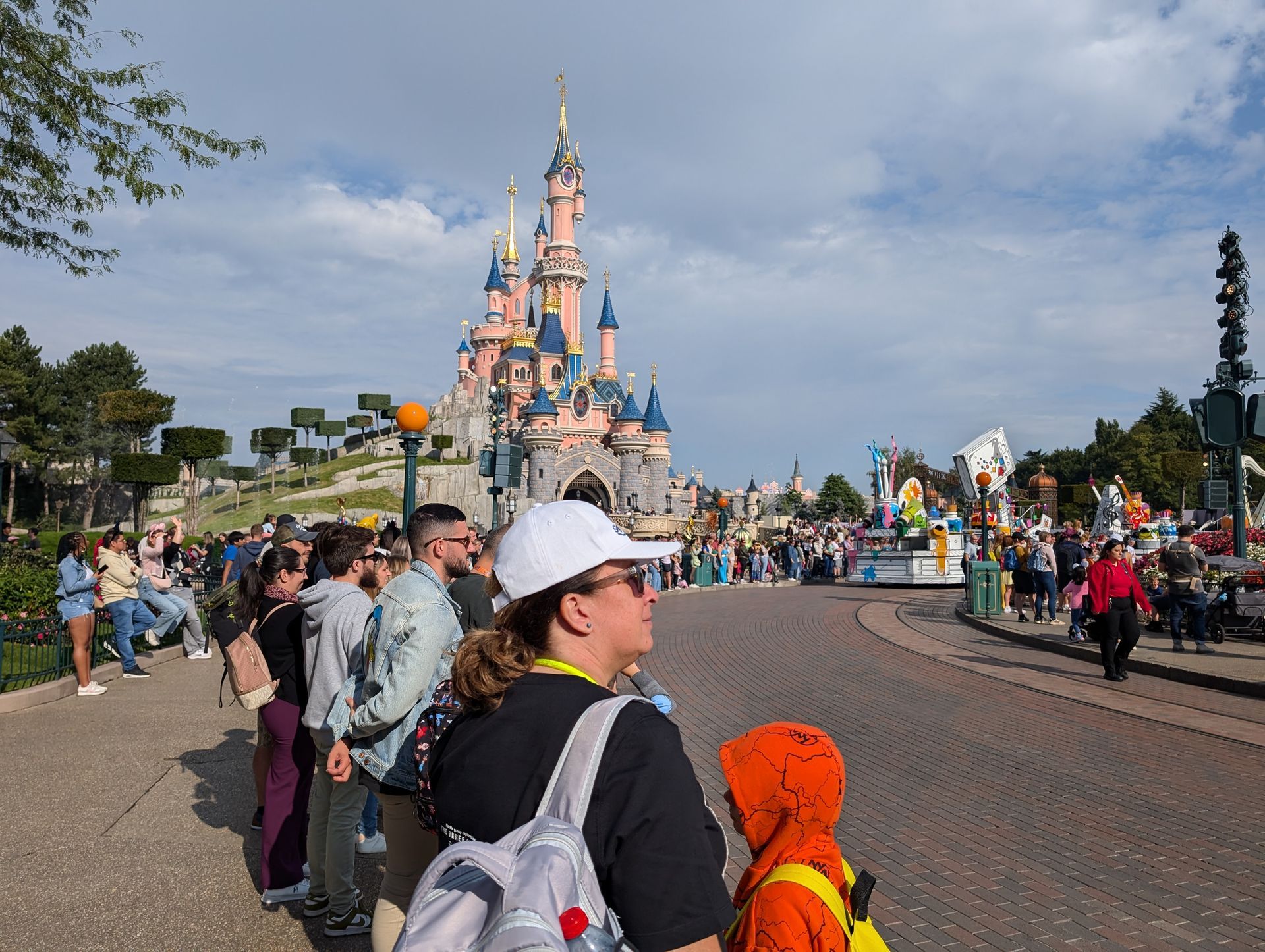 People watching a parade at Disneyland Paris with Sleeping Beauty Castle in the background. Blue sky, colorful floats.