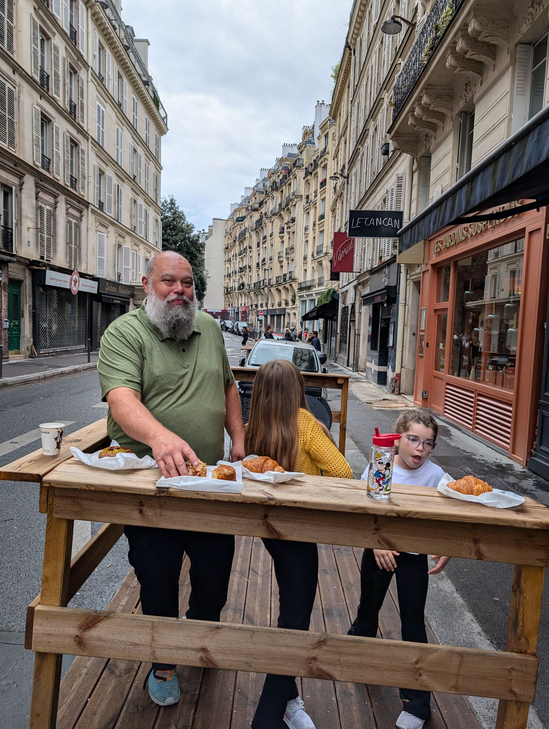 Man and children at outdoor table with pastries in a European street setting.