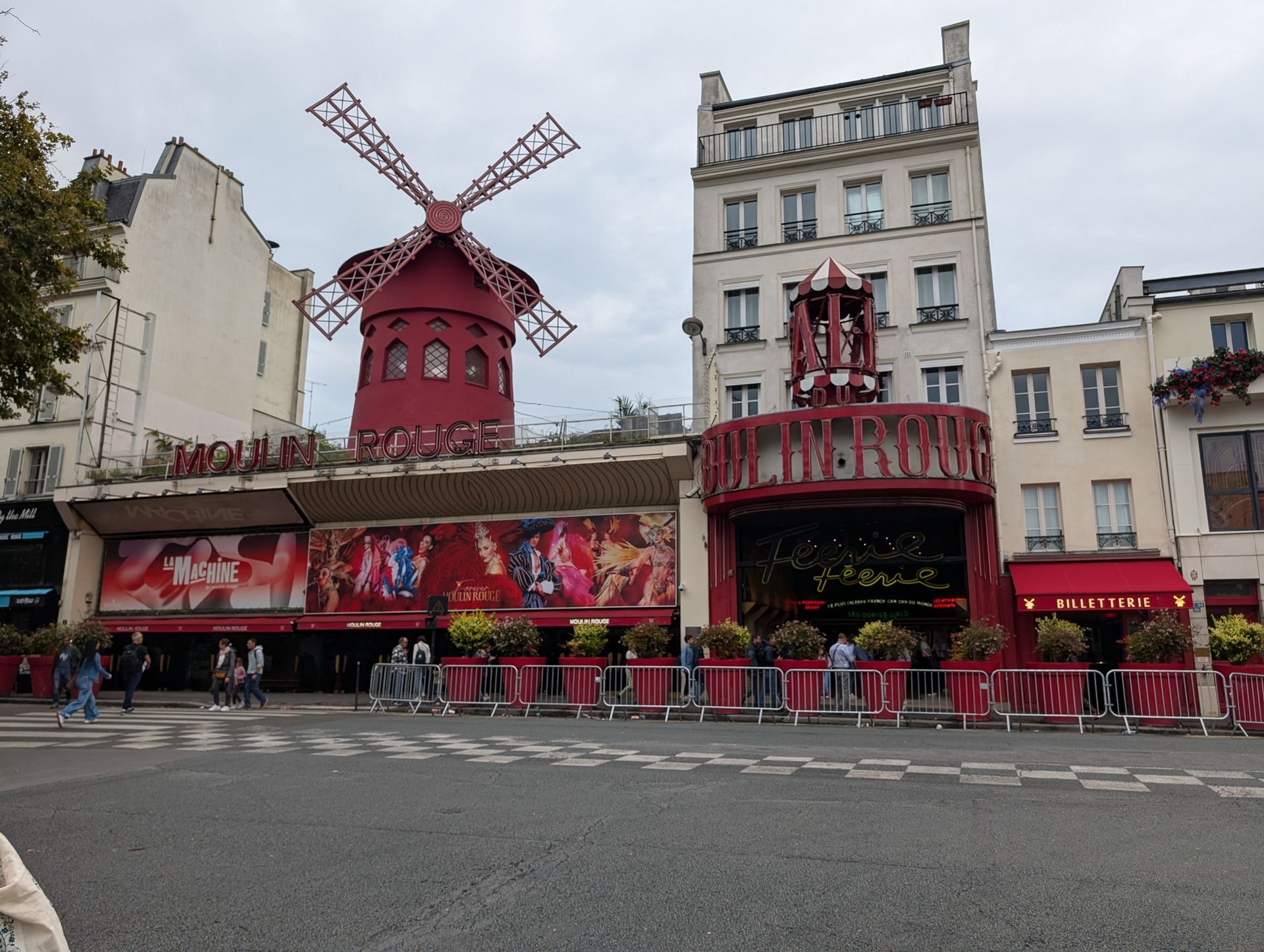 Moulin Rouge cabaret building in Paris, France. Red windmill, entrance, and posters. People on the street.