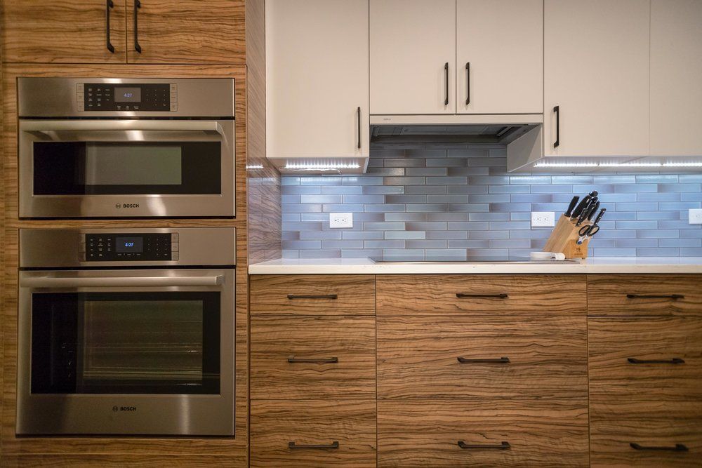 Modern kitchen with bamboo-style cabinets, white upper cabinets, and stainless steel oven appliances.