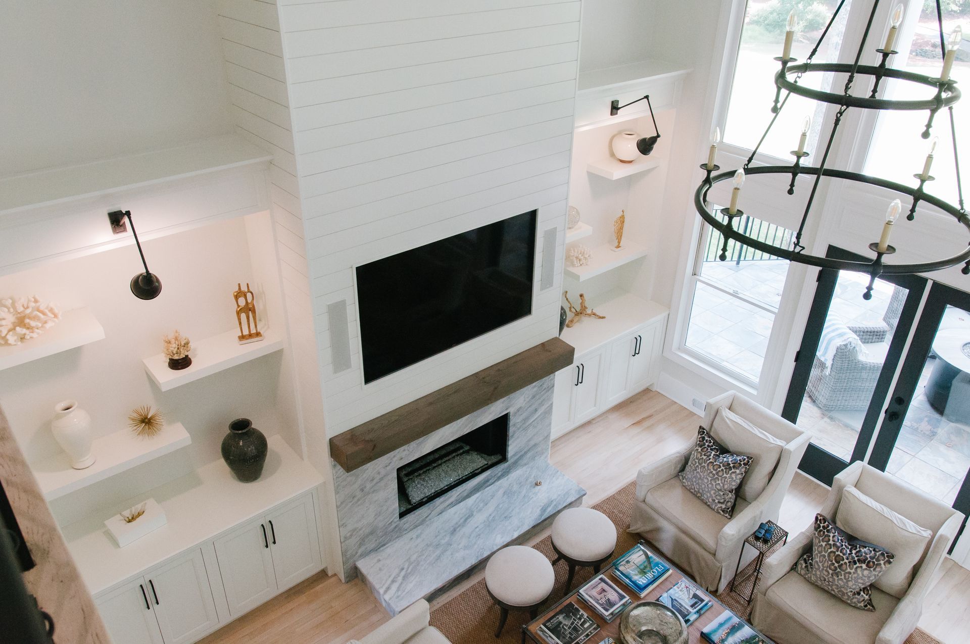 High-angle view of a bright living room with a fireplace, TV, built-in shelving, and a chandelier.