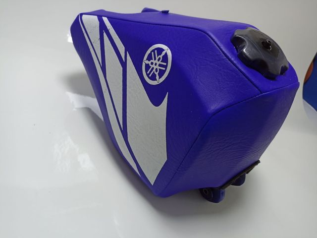 Depósito de combustible azul para motocicleta Yamaha, con gráficos blancos y tapón negro, sobre una superficie blanca
