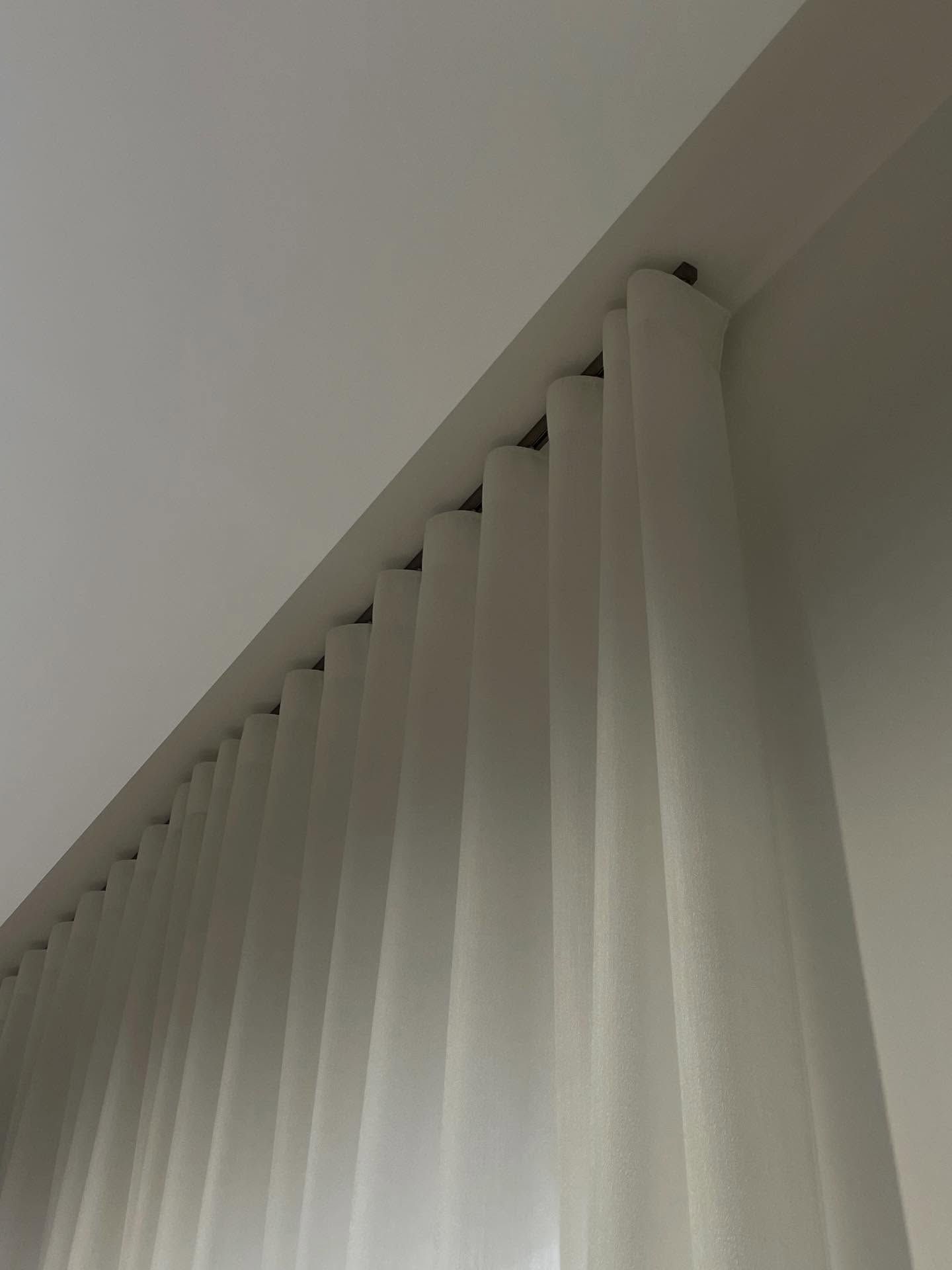 Tende bianche appese a un binario sul soffitto, viste da un'angolazione bassa.