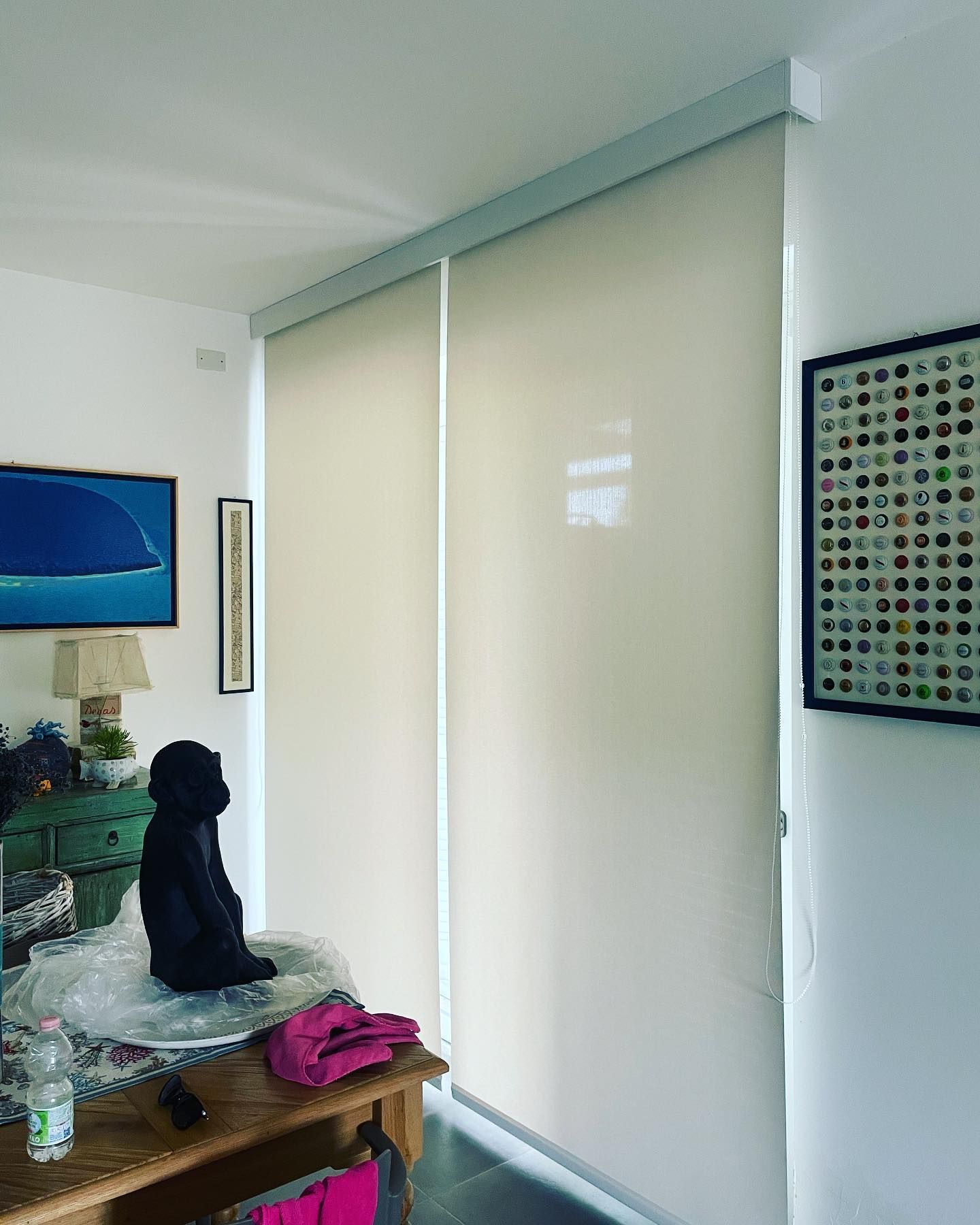 Tende a rullo beige in una stanza con opere d'arte, un tavolo e una scultura nera.