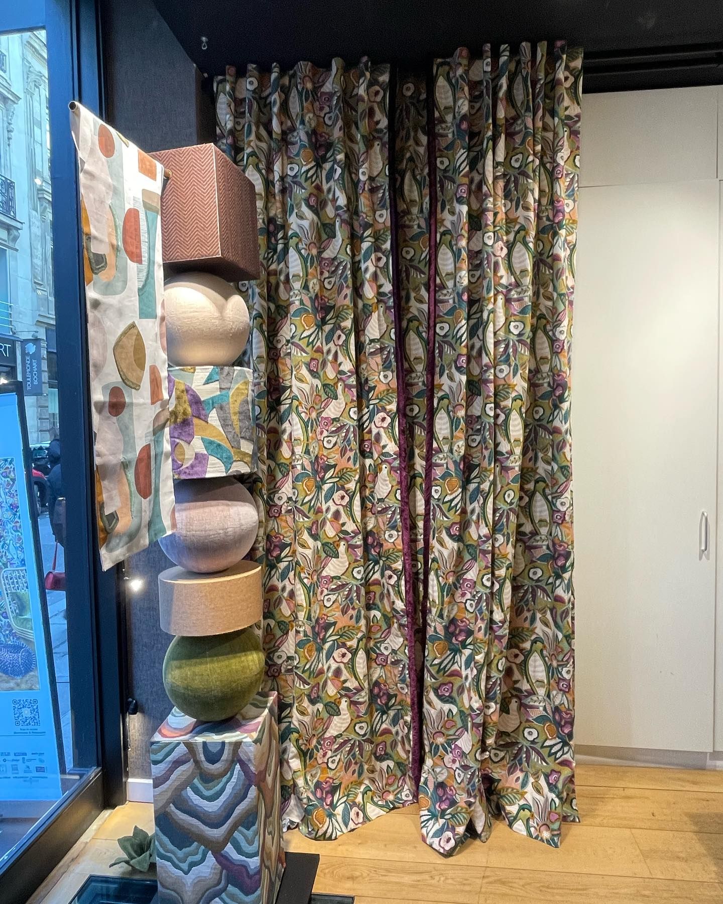 Esposizione di tende a fantasia e oggetti decorativi impilati nella vetrina di un negozio.