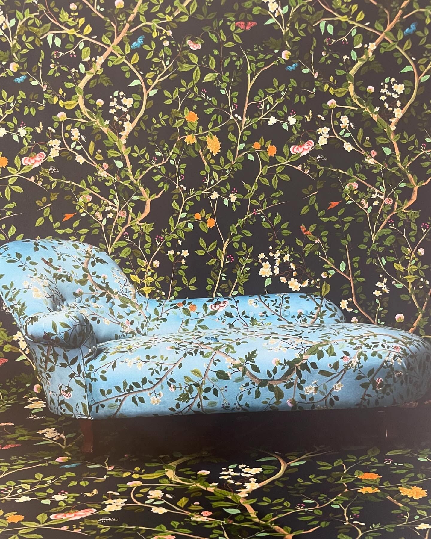 Chaise longue blu con motivi floreali di fronte a una parete e a un tappeto con motivi floreali.