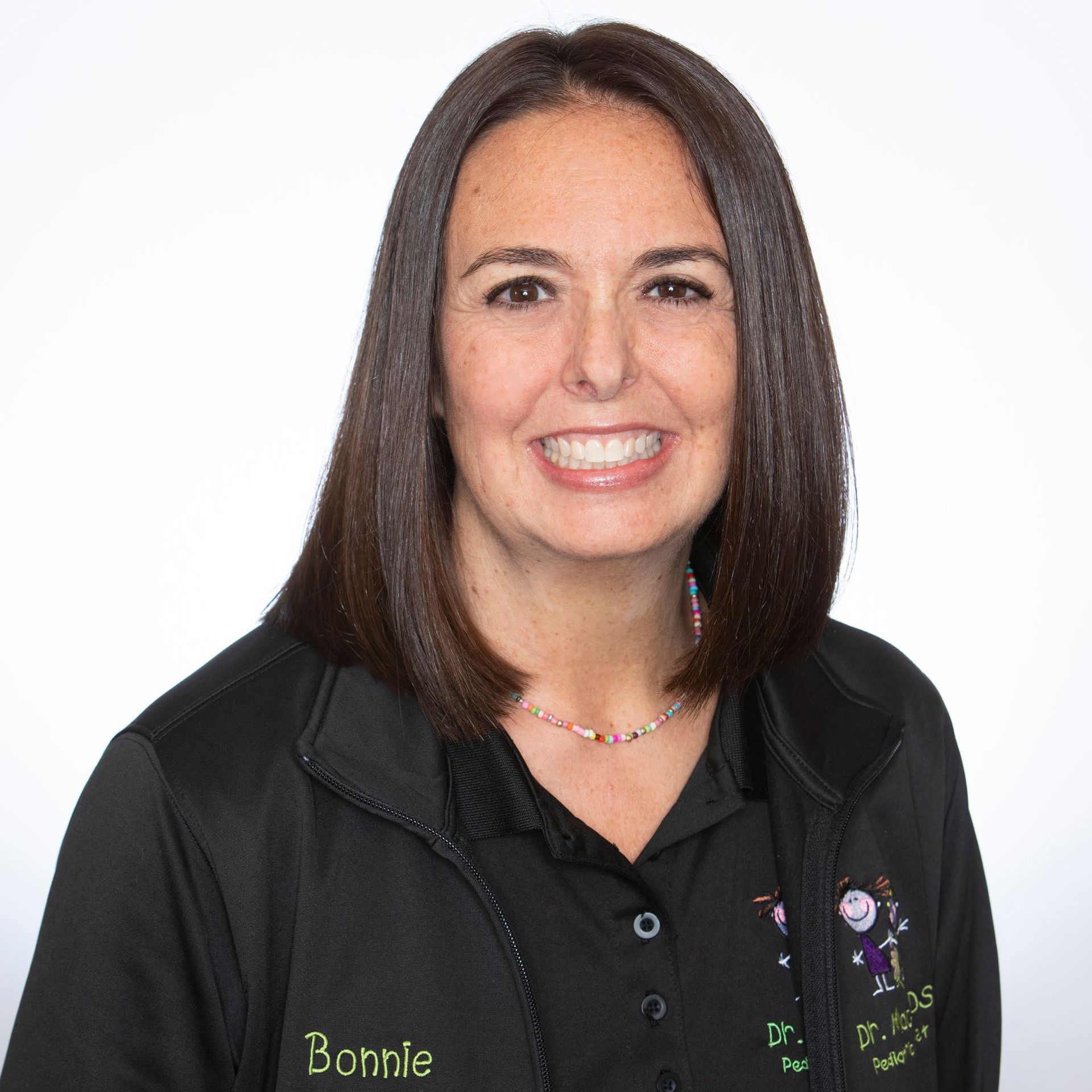 A woman wearing a black shirt and a black vest is smiling for the camera.