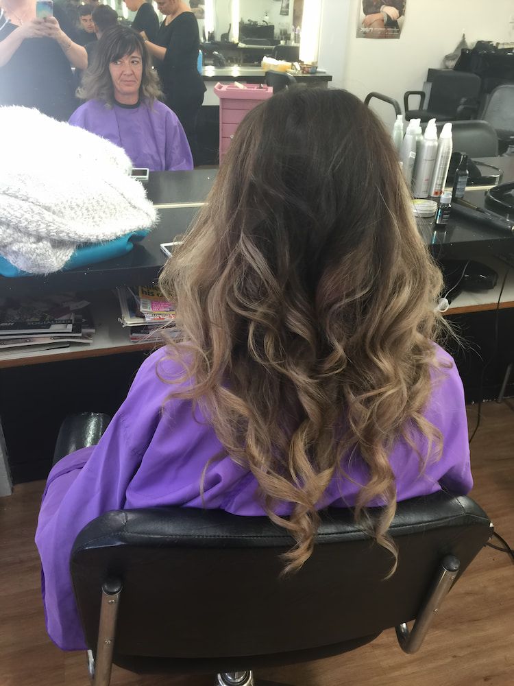 A Woman In A Purple Cape Is Sitting In A Chair In A Salon — Howard Street Hair Studio In Nambour, QLD