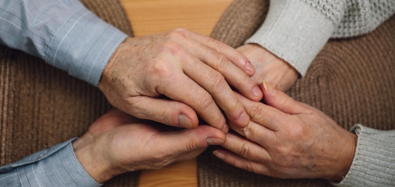 Older adult's hands gently held by another person, symbolizing long-term care support.