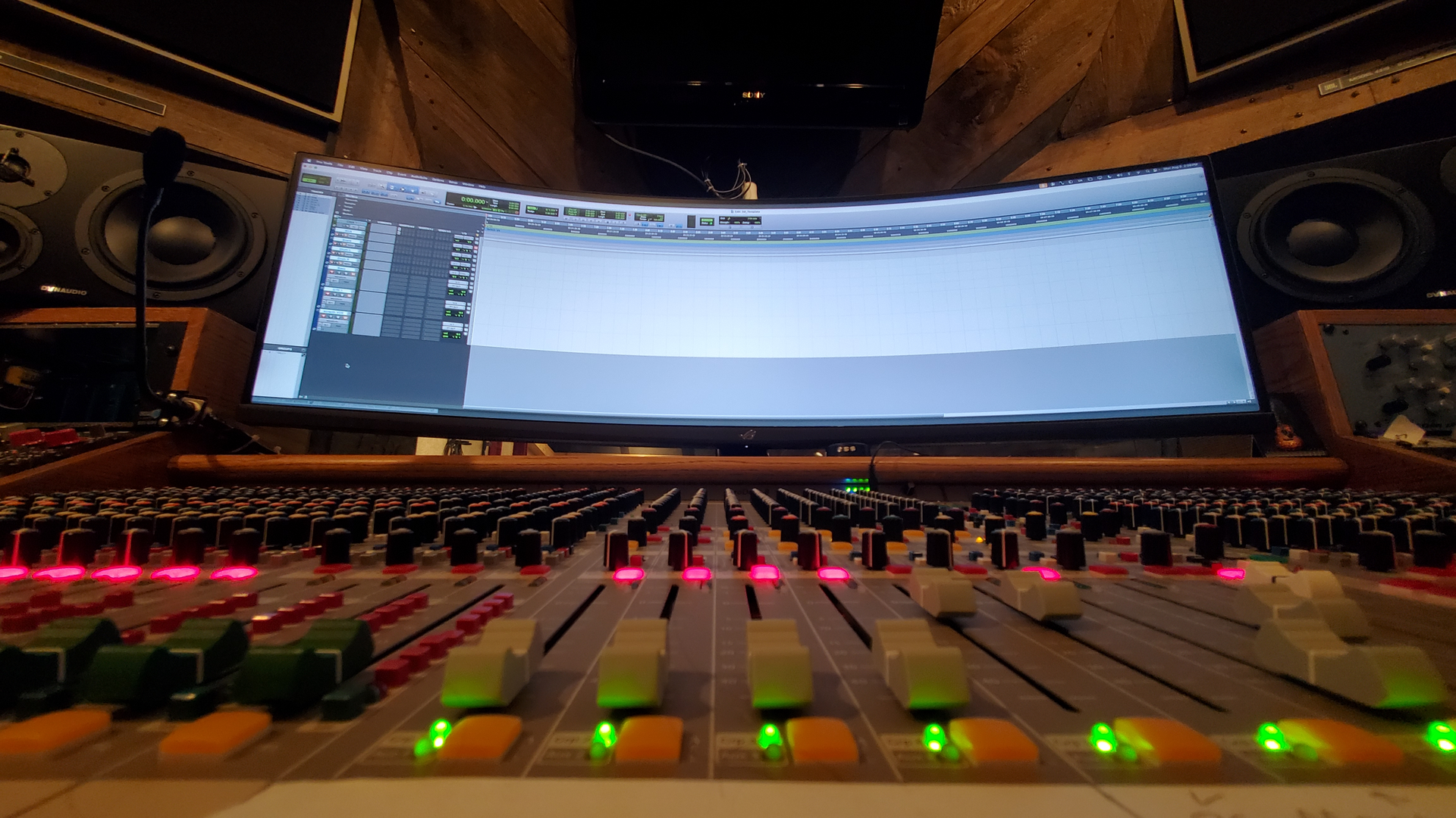 A professional recording studio featuring a large curved monitor displaying audio software above a mixing console.
