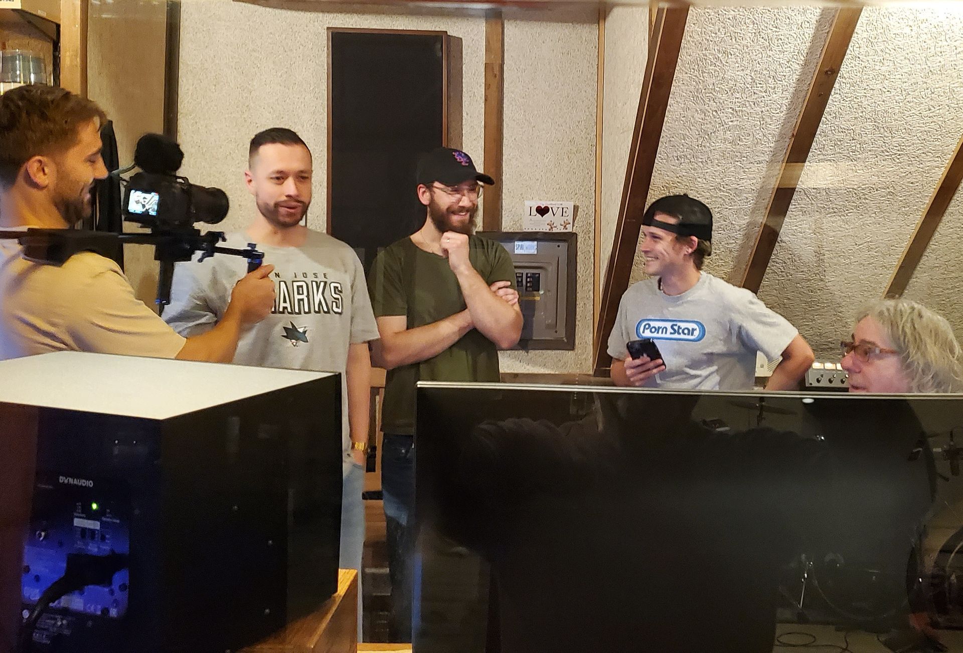 Band members in control room talking and smiiling, one person with a video camera aimed at them
