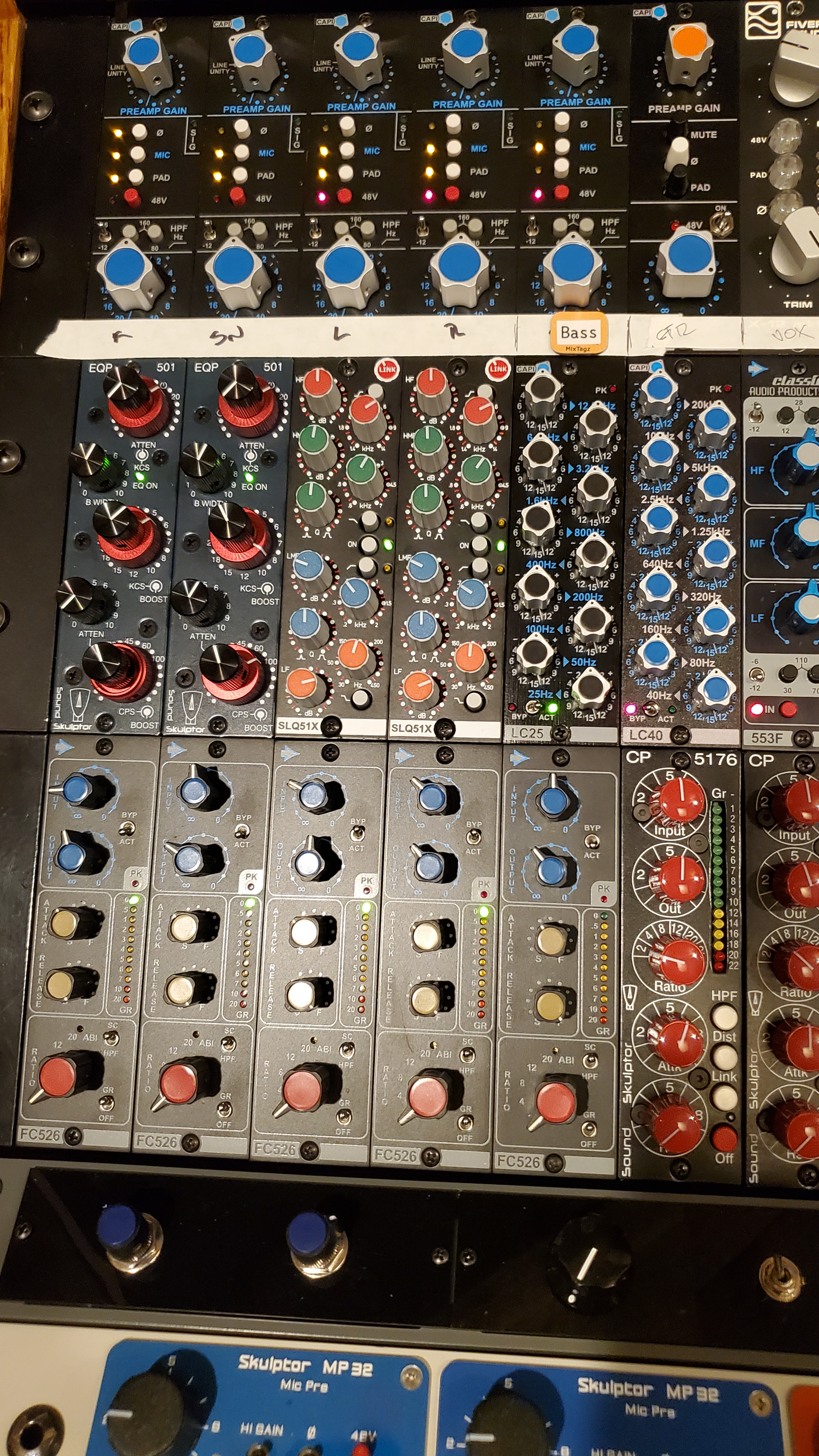 A vertical view of professional audio rack-mount studio equipment with numerous knobs, buttons, and status lights.