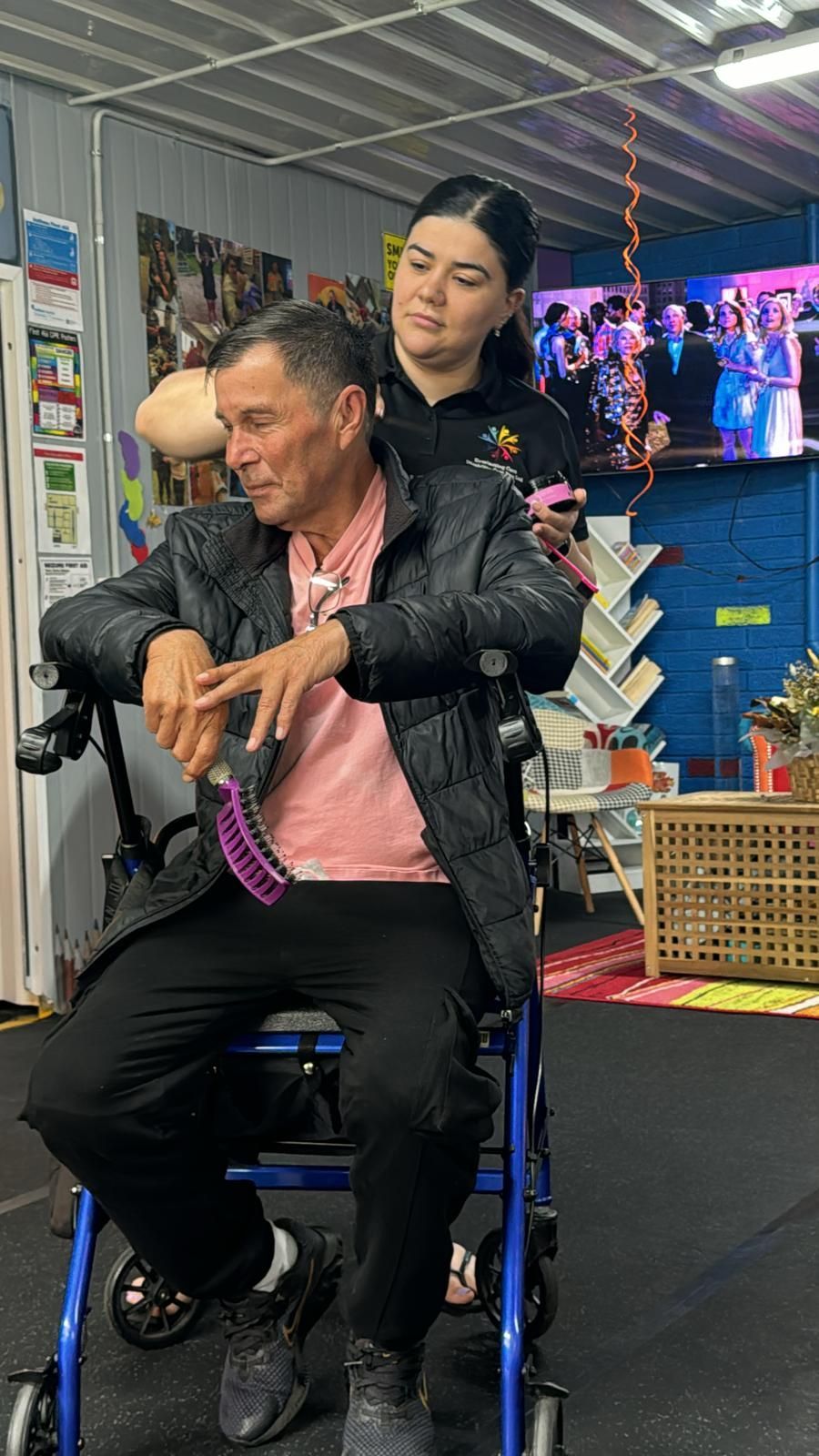 A woman is helping a man in a wheelchair with a walker.