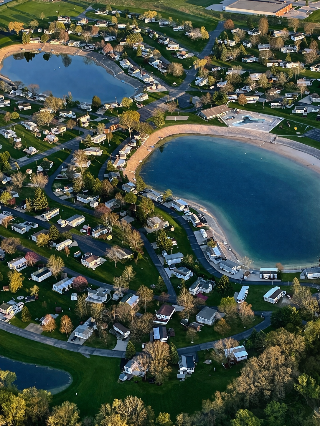Aerial view of a residential neighborhood featuring two small lakes with sandy beaches, surrounded by houses and trees.