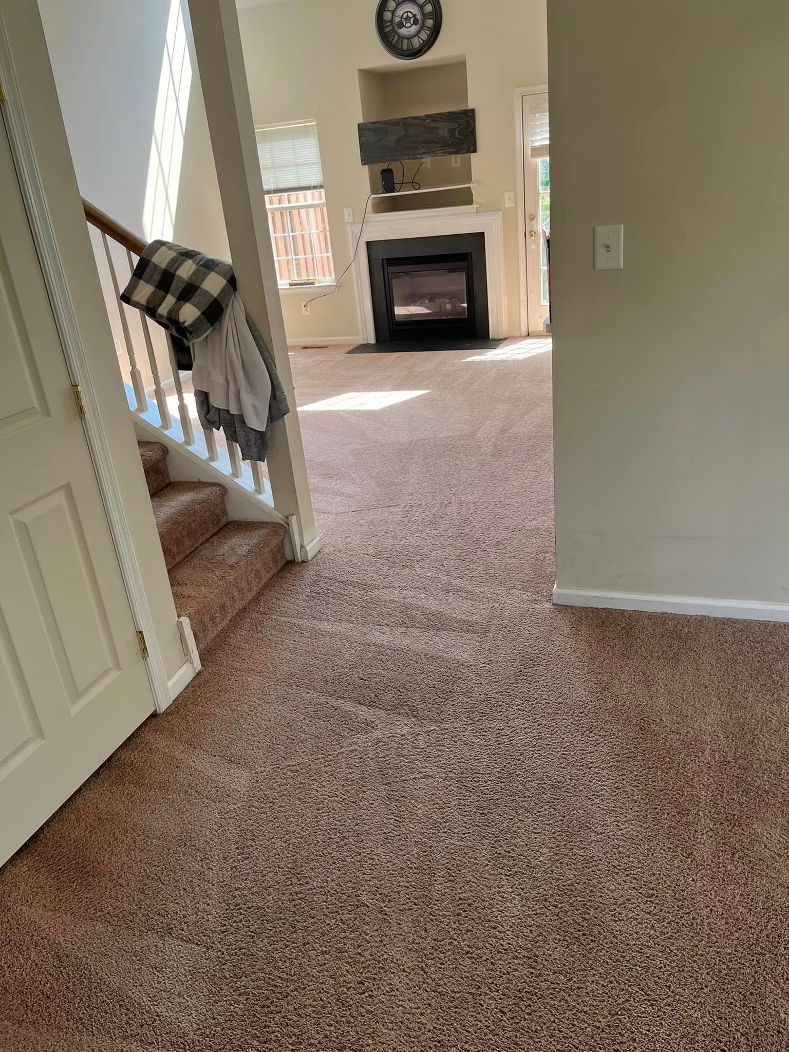 A living room with a fireplace and stairs and a carpeted floor.