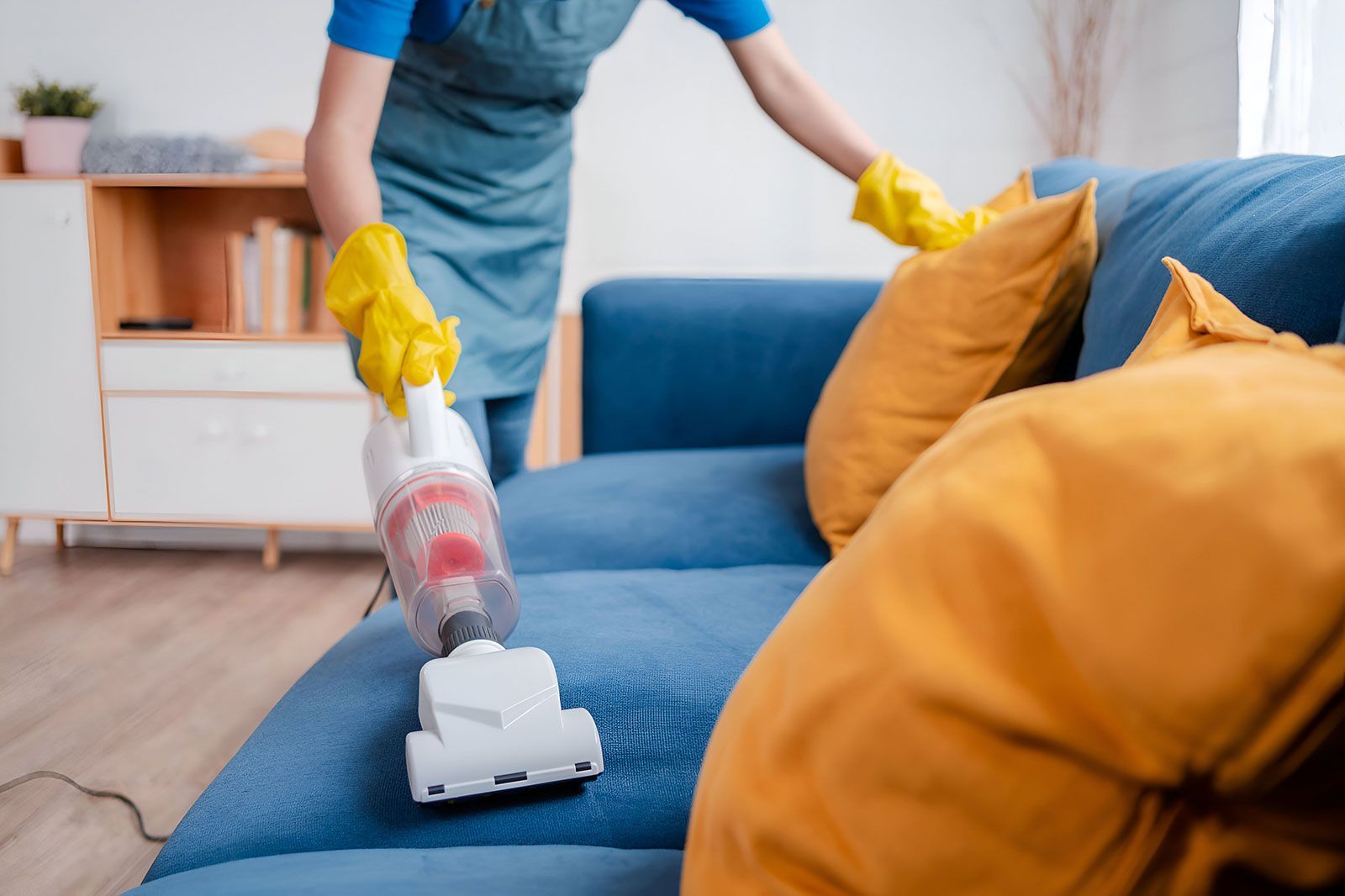 A woman is cleaning a blue couch with a vacuum cleaner.