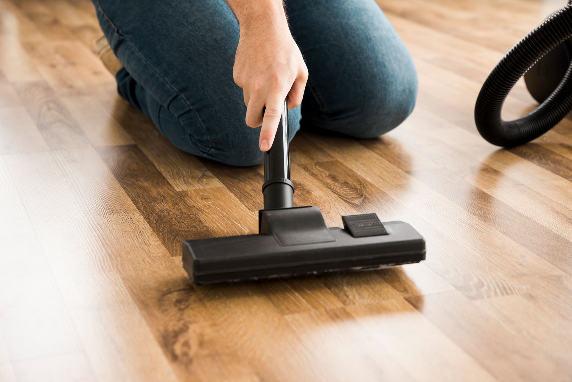 A person is cleaning a wooden floor with a vacuum cleaner.