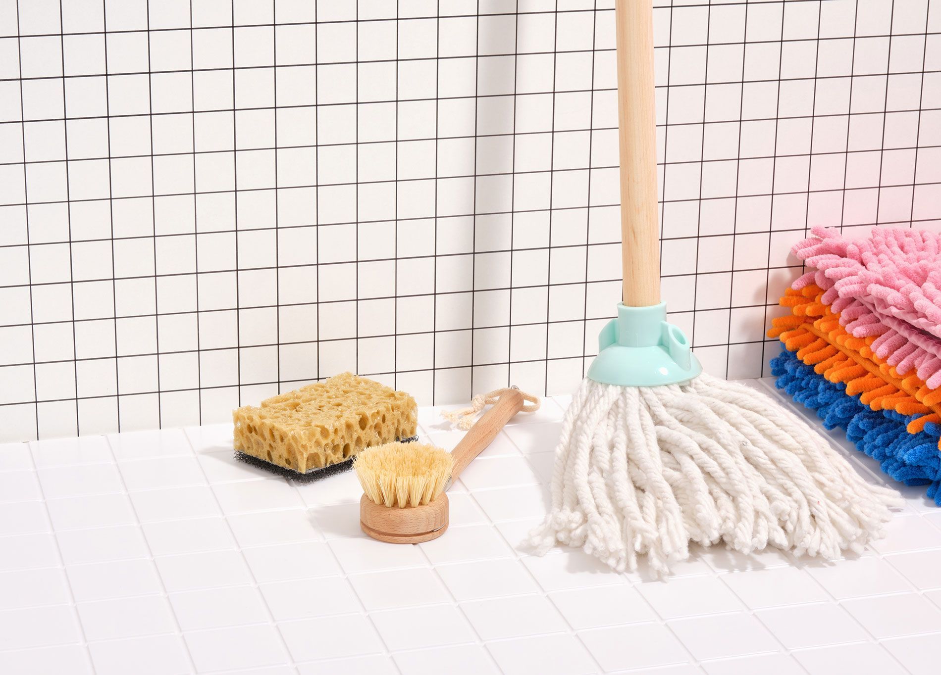 A mop , sponge , and brush are sitting on a tiled floor.
