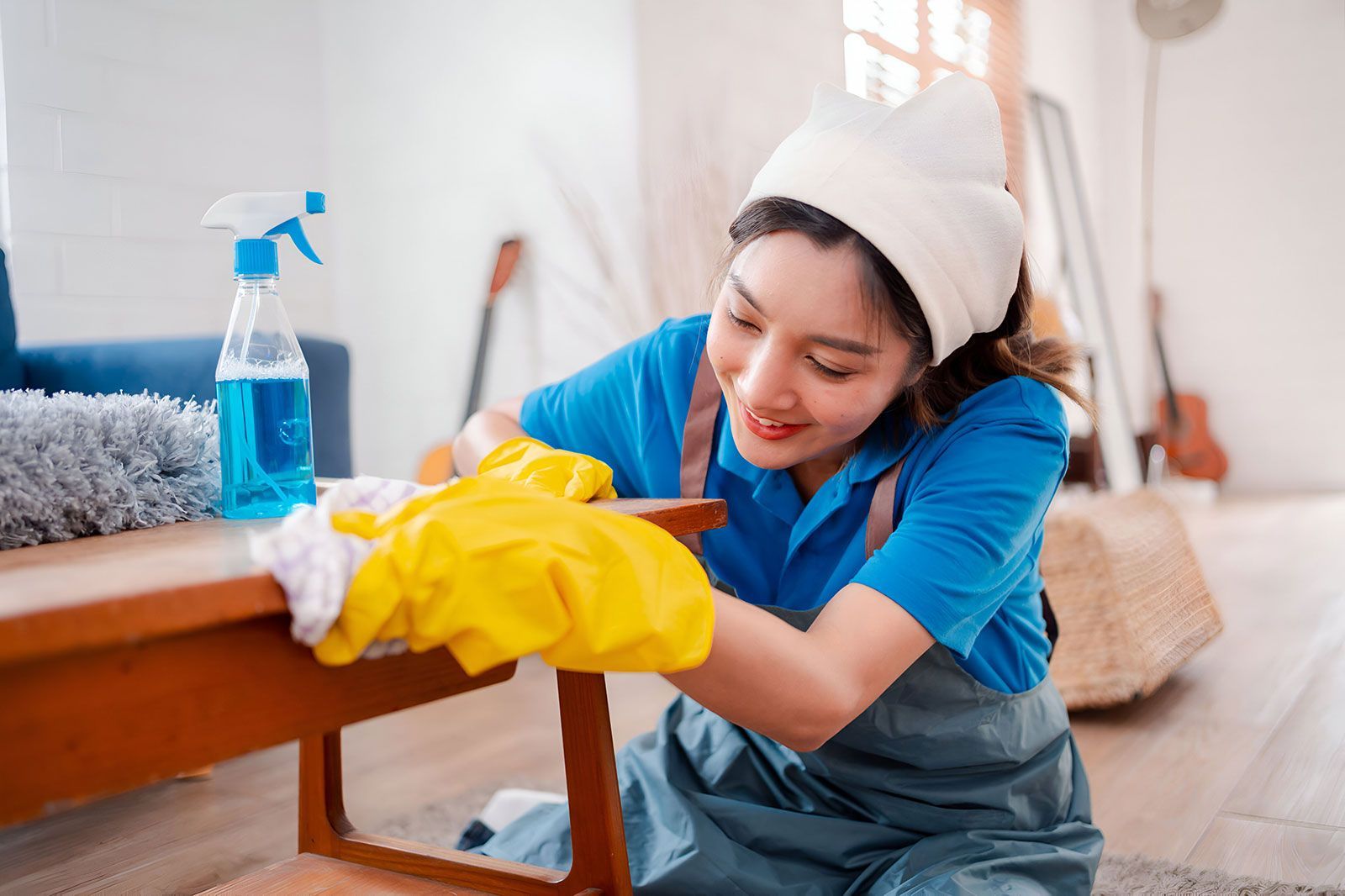 A woman is cleaning a wooden table in a living room.