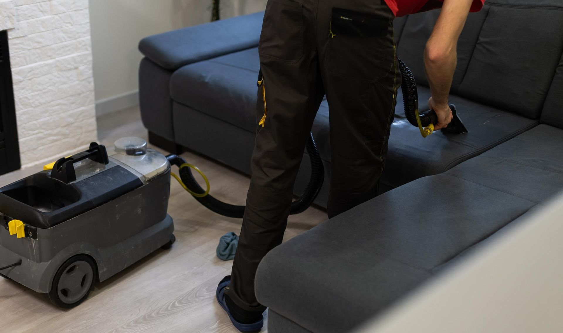 A man is cleaning a couch with a vacuum cleaner in a living room.