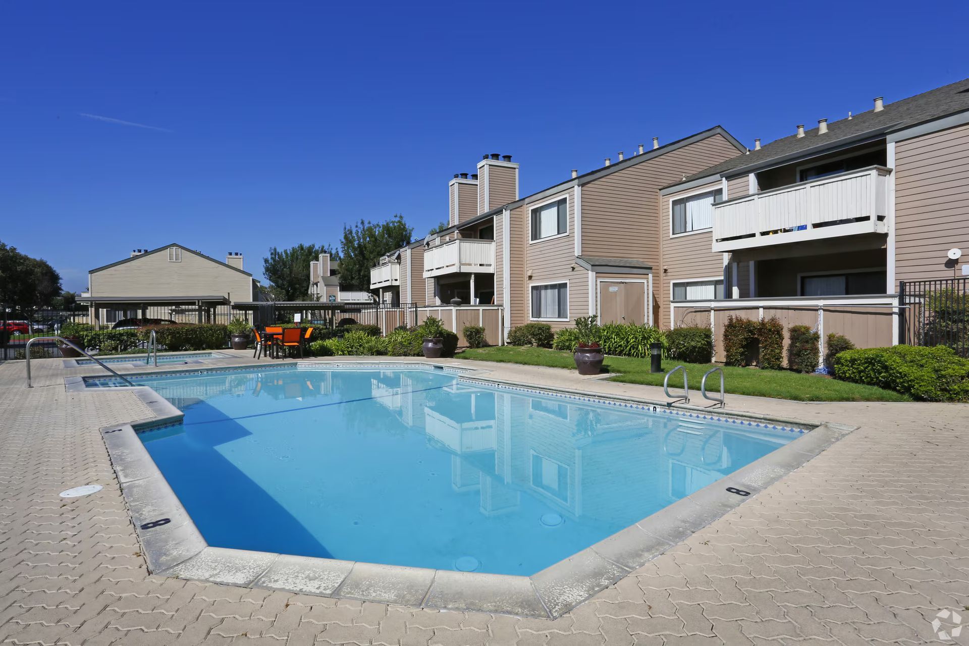 Apartment courtyard with a blue swimming pool and lounge chairs under a clear sky