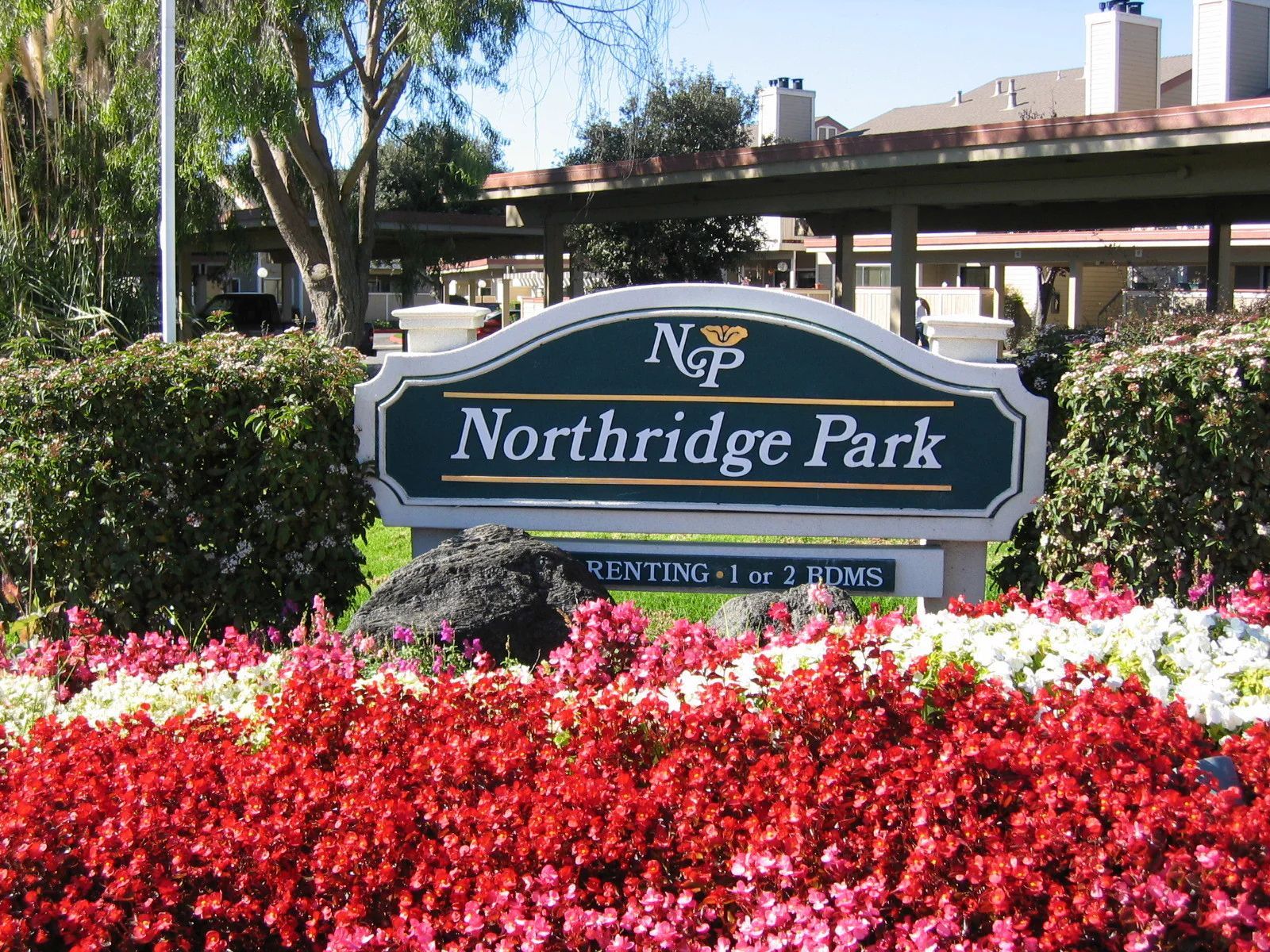 Northridge Park entrance sign amid red and white flowers, with trees and an overpass behind