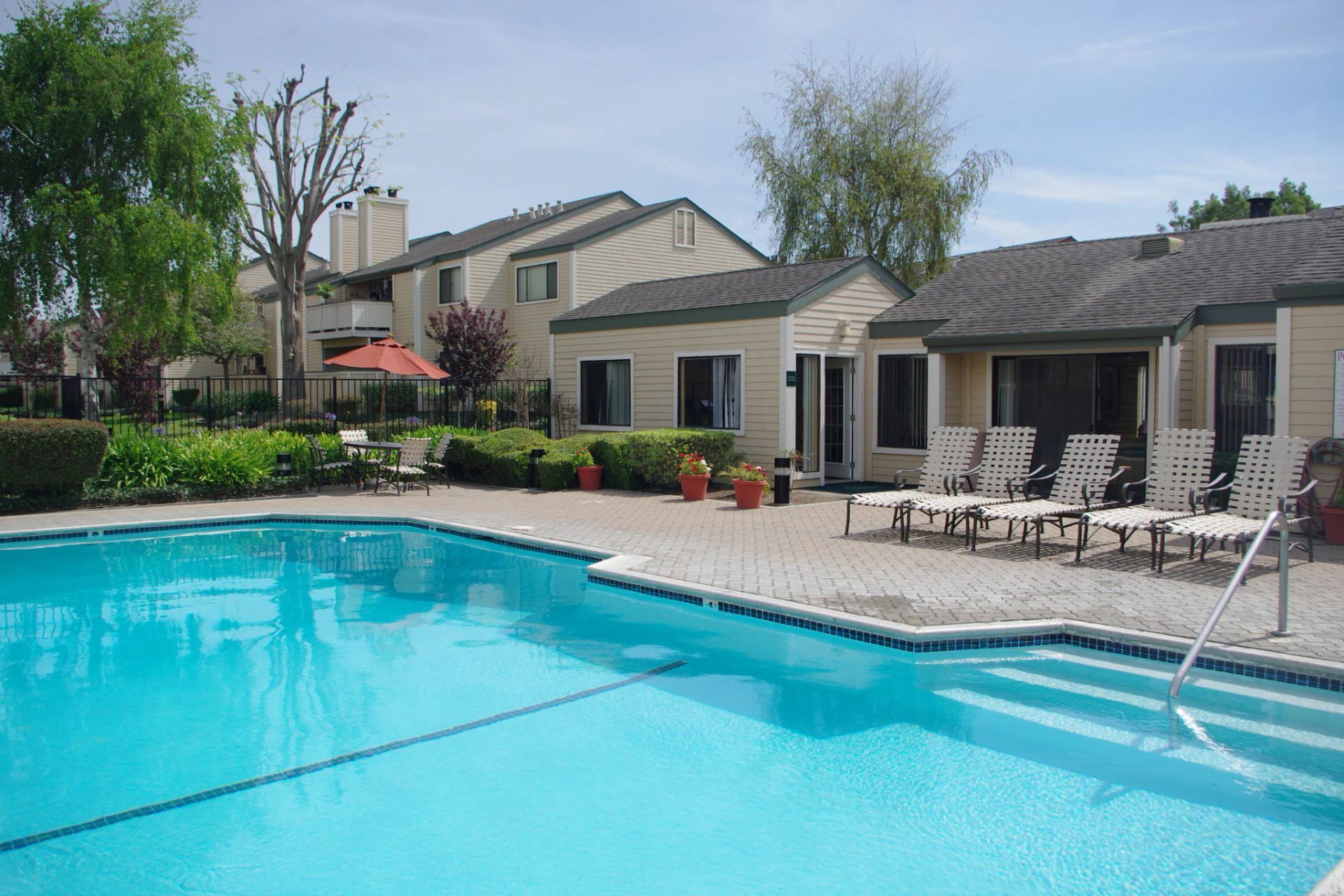 Apartment pool with turquoise water, lounge chairs, and beige buildings on a sunny day