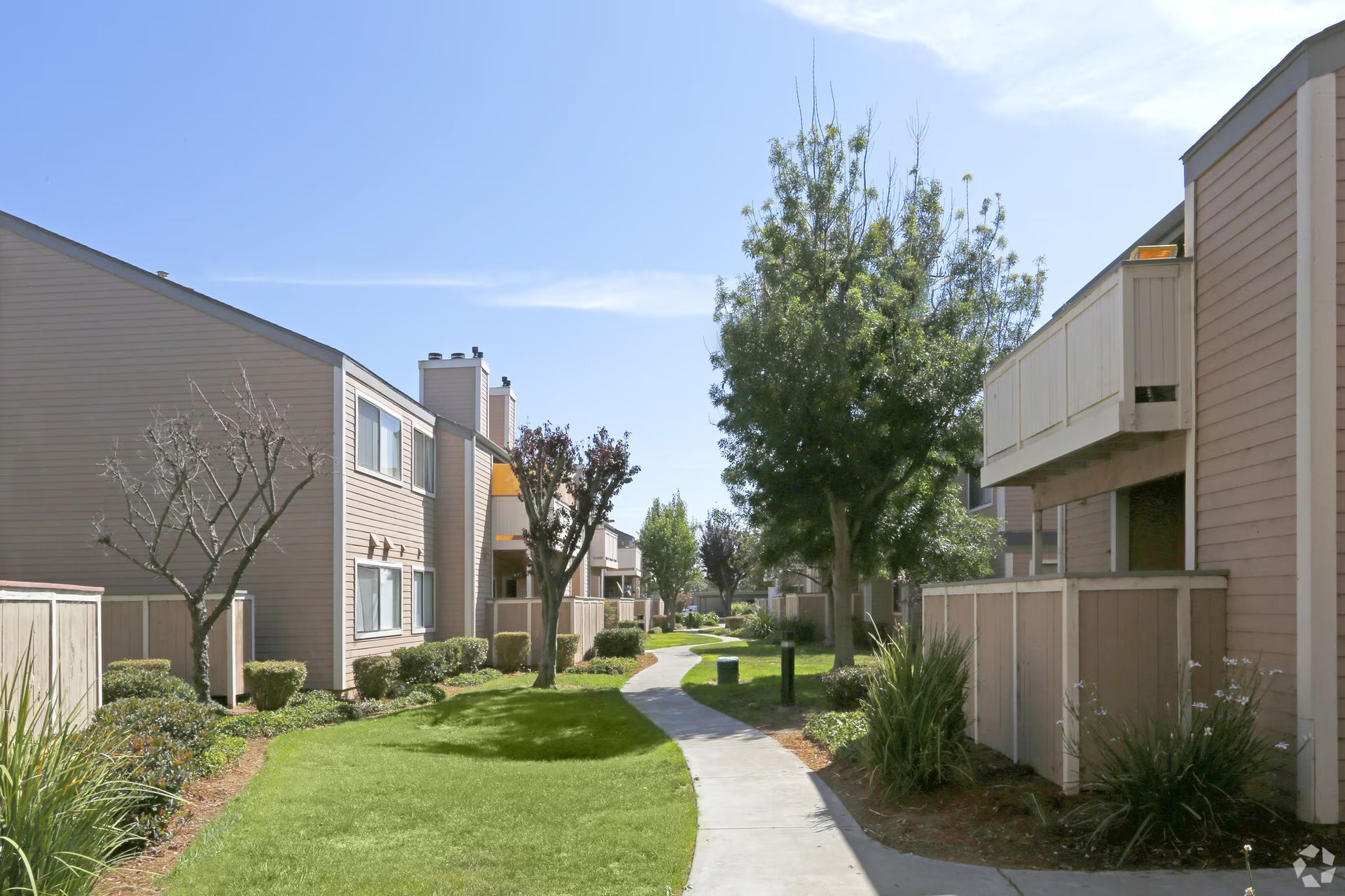 Residential courtyard with townhouses, a curving path, green lawn, and trees under a clear sky