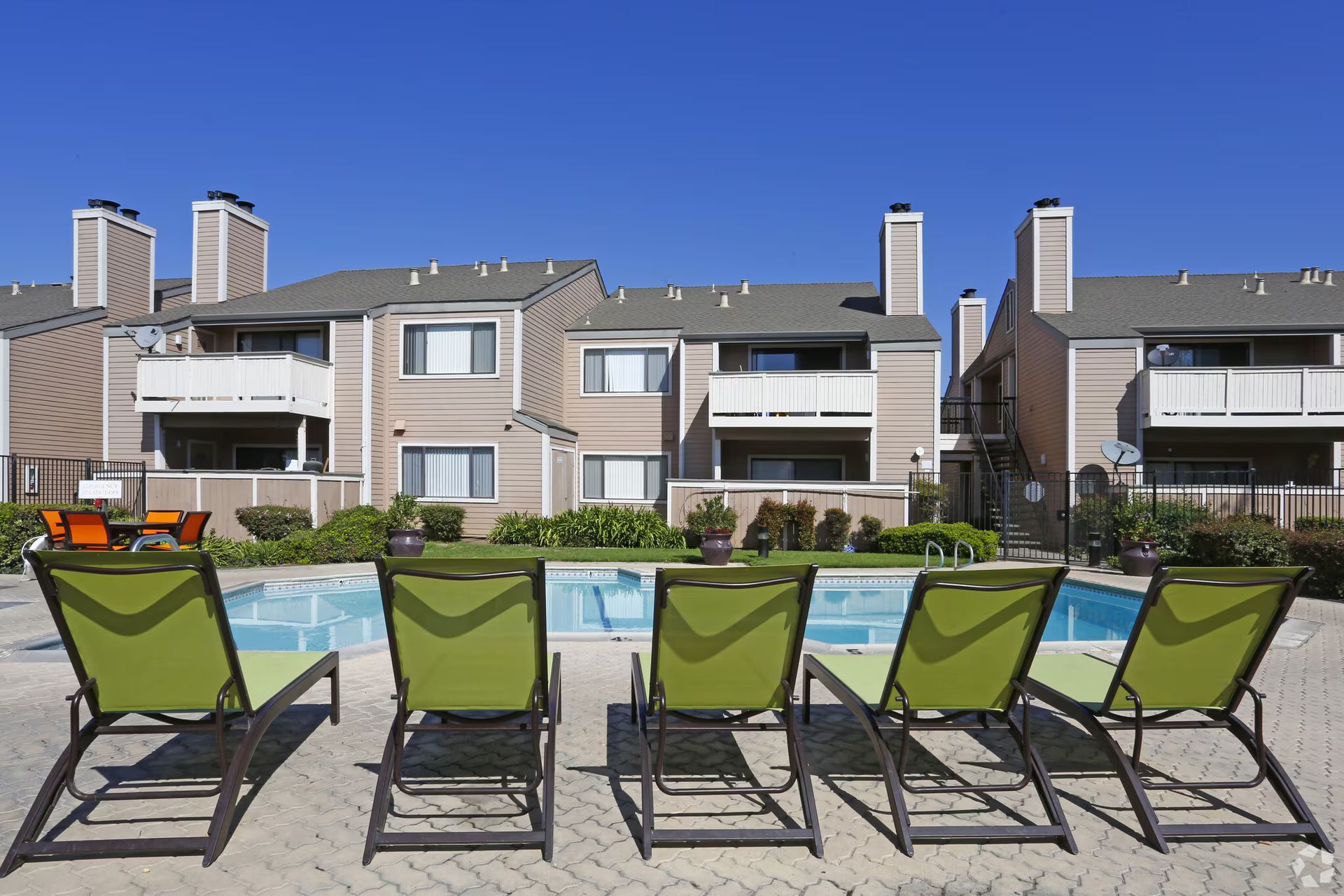 Poolside lounge chairs facing modern apartment buildings under a clear blue sky