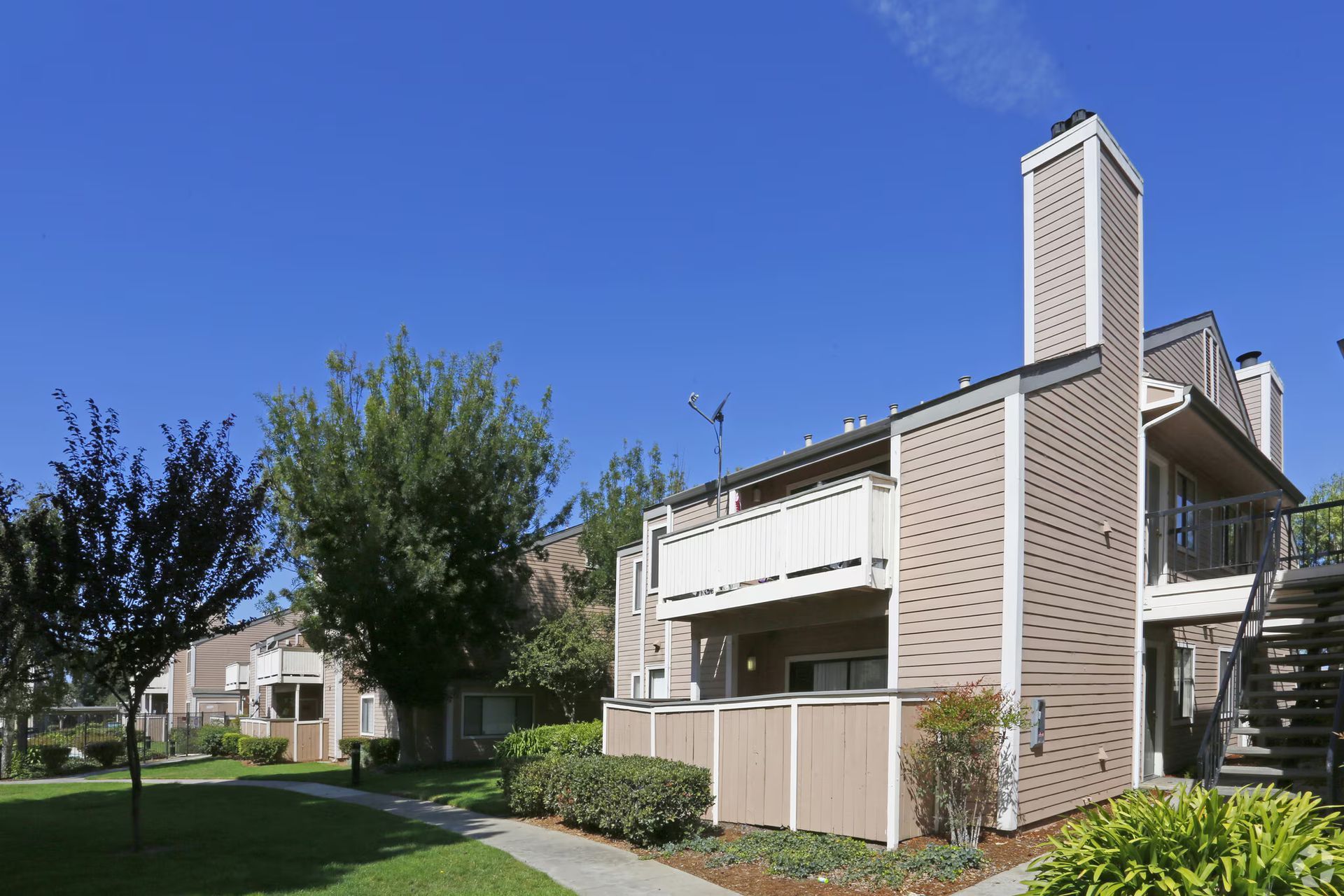 Apartment building with balconies and a tall chimney under a clear blue sky