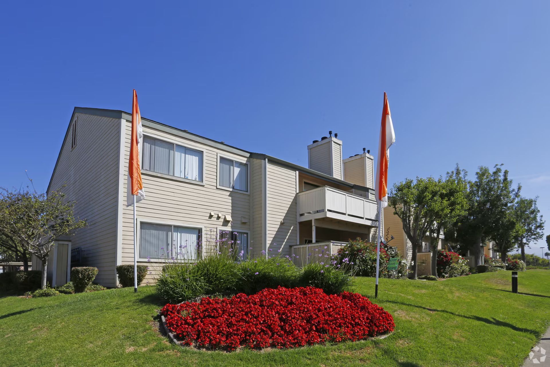 Apartment building with balconies, red flower bed, and flags on a sunny green lawn